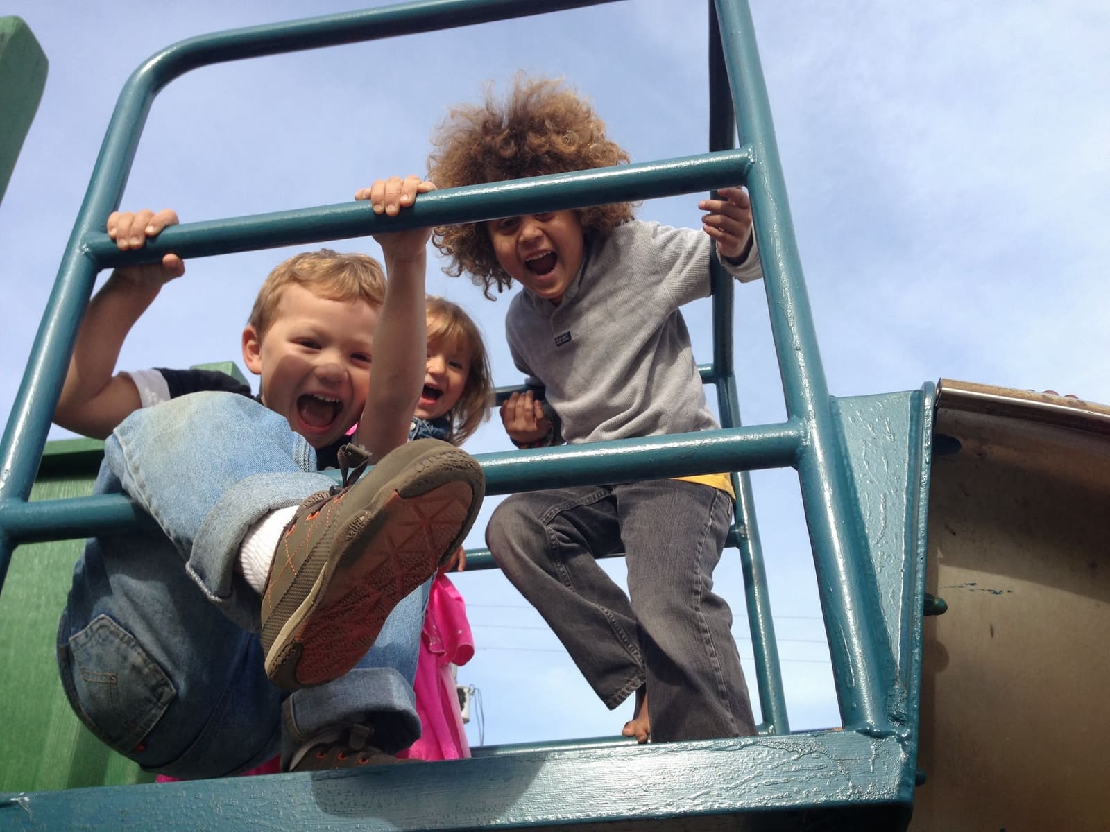 Three children laughing on the steps of the climbing structure