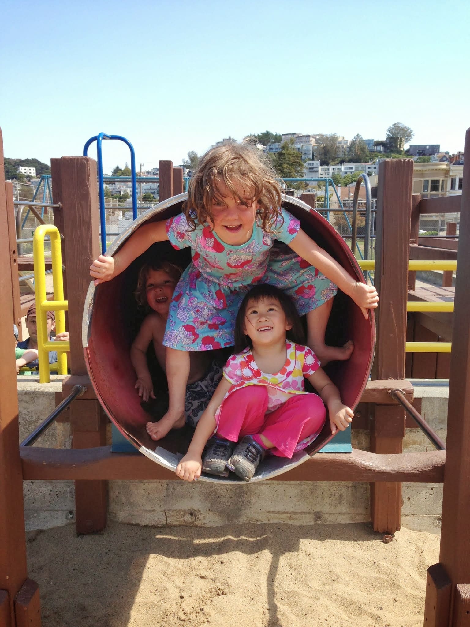 Three children sitting inside the play tunnel, smiling out at the camera