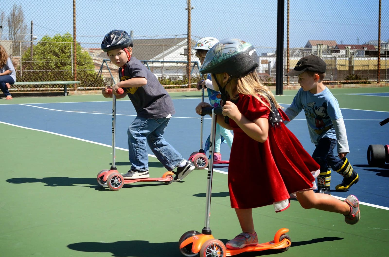 Four children in helmets riding scooters across the blacktop