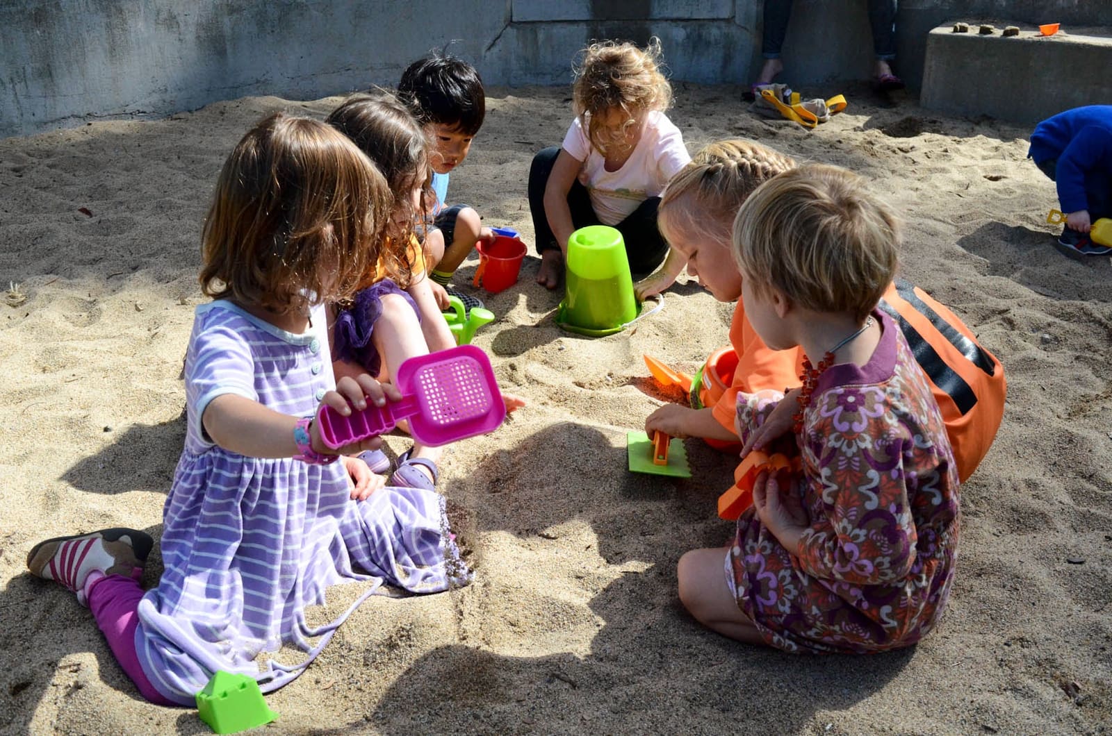 Six children kneeling in the sandbox filling buckets and sifters