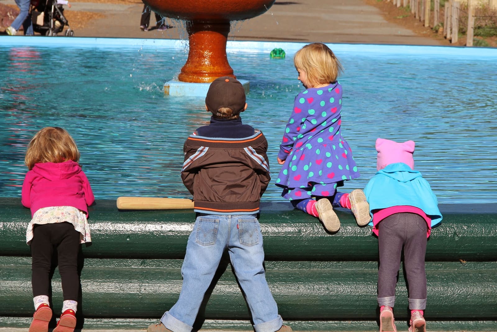 Two children standing at the edge of a fountain, watching the water
