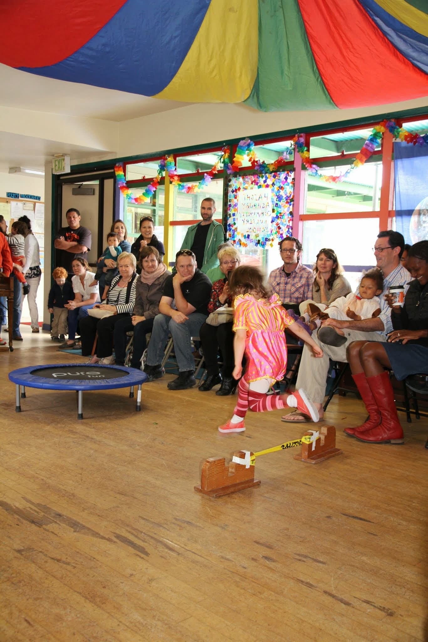 Parents seated around the room watching a child perform at a school event