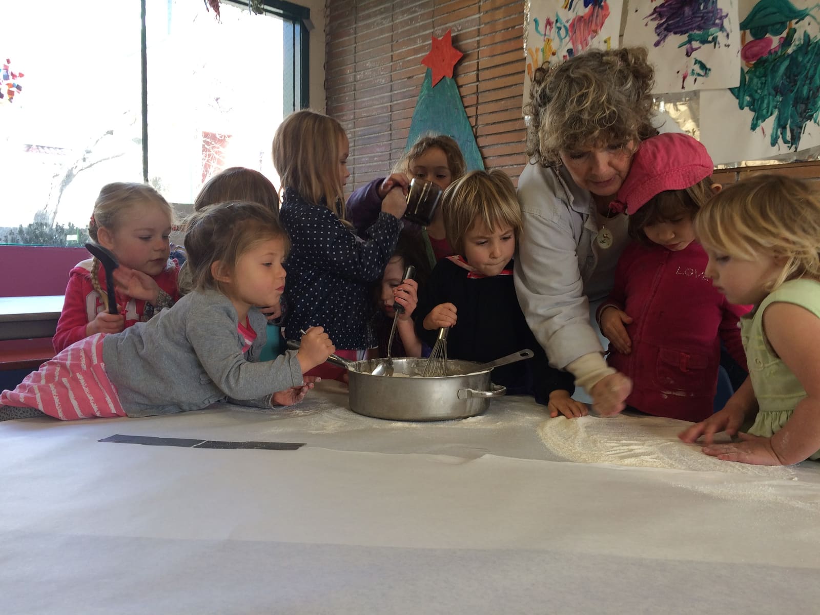 A teacher and a group of children gathered around a mixing bowl during a cooking project