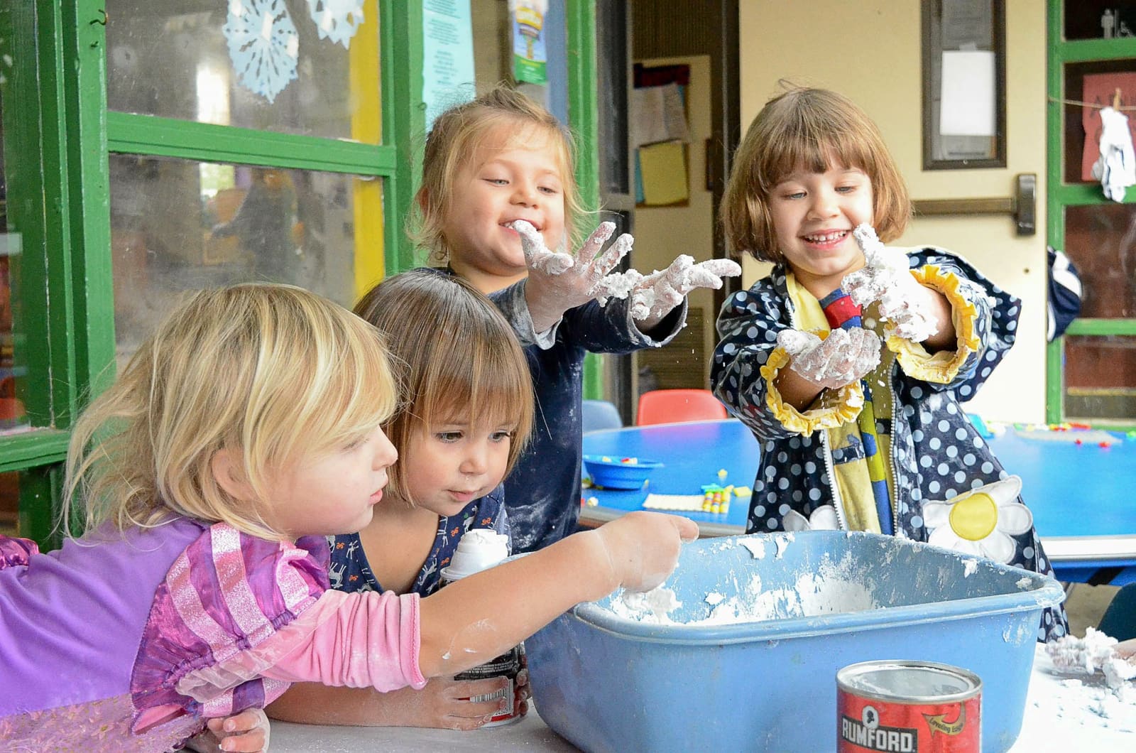 Four children with flour on their hands mixing dough in a tub at the sensory table