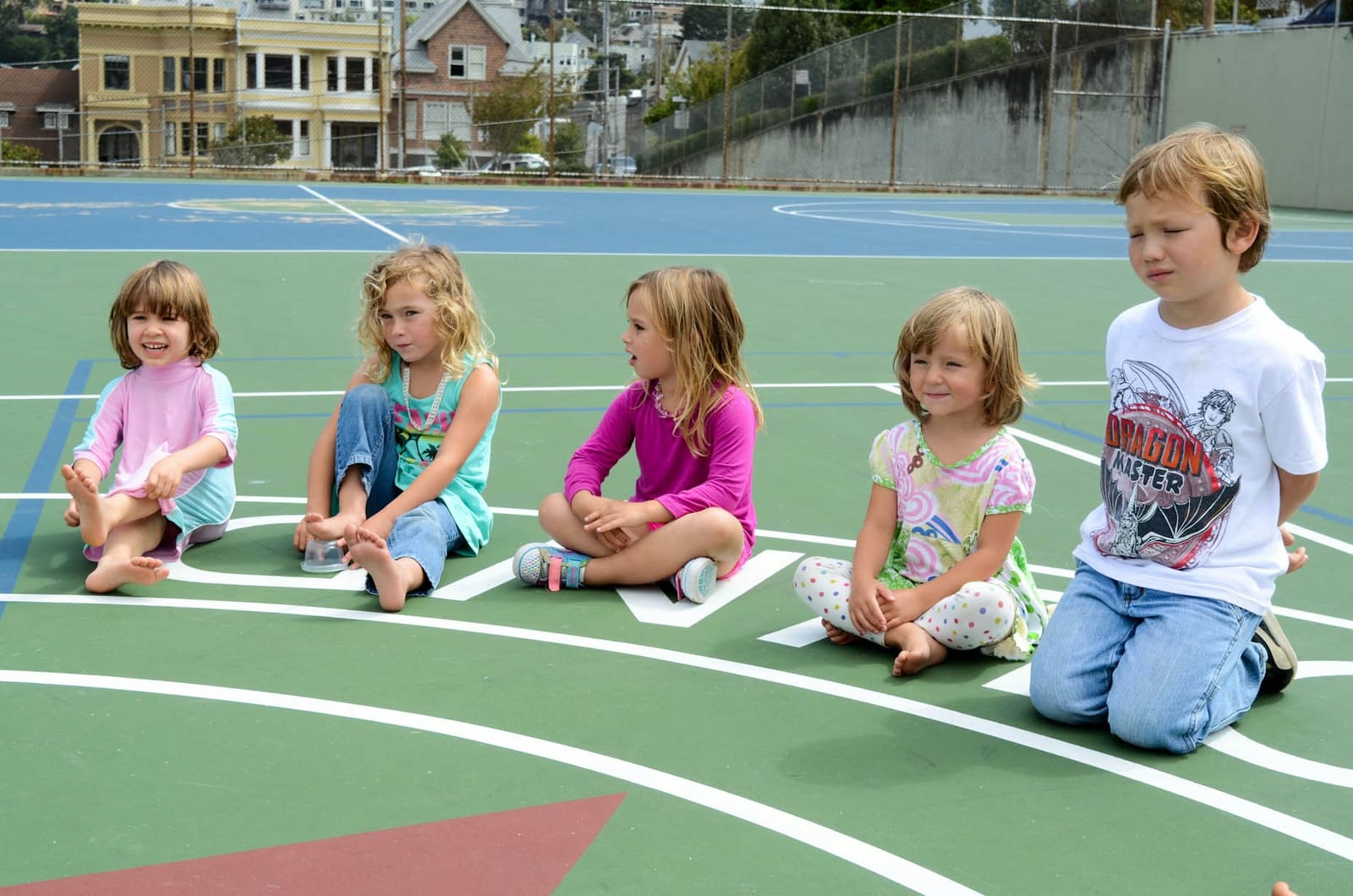 Three children sitting cross-legged on the blacktop during circle time outdoors
