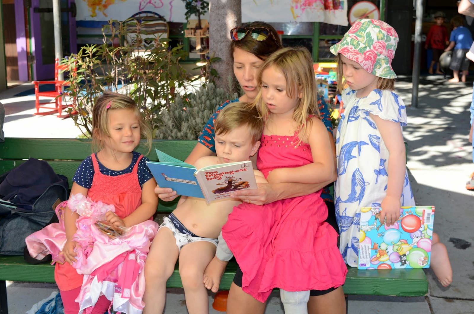 A teacher reading a picture book to three children sitting with her outside