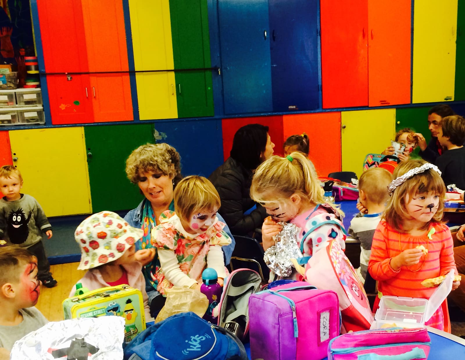Teachers and children unpacking lunch boxes in the rainbow-cupboard room