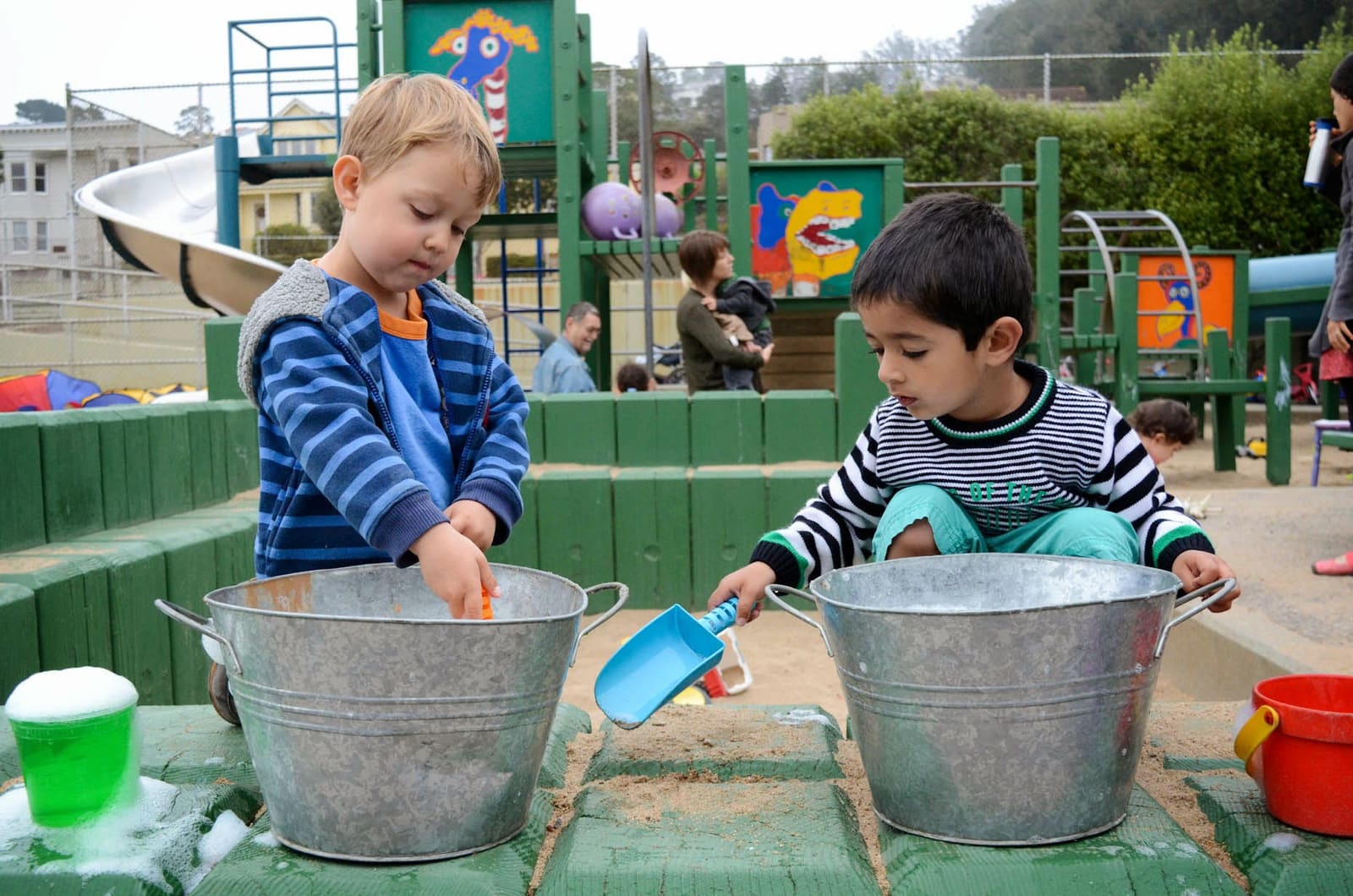 Two children scooping sand into metal tubs at the sand table